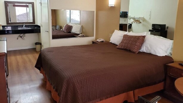 Habitación de hotel con una cama grande, una mesita de noche, un escritorio con silla, un espejo y una ventana.