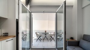 En moderne lejlighed med balkon, spisebord og stole, en sofa samt et køkken med skabe og bordplade.