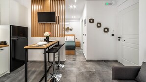 Ett modernt hotellrum med ett litet pentry, en säng med ett grönt överkast, en tv som är monterad på en träpanel och en liten sittgrupp med en stol och ett bord.