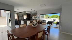 Une cuisine moderne dotée d’un îlot central, d’un coin repas avec une table et des chaises en bois, et offrant une vue sur un jardin luxuriant grâce à de grandes portes coulissantes.