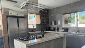 Une cuisine moderne dotée d’un îlot central, d’appareils électroménagers en acier inoxydable et offrant une vue sur l’extérieur.