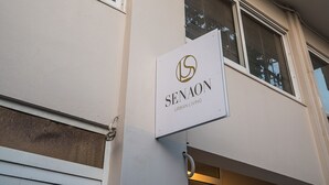 Rakennuksessa on kyltti, jossa lukee ”SENAON URBAN LIVING”, ja siinä on ikkuna, jossa on sälekaihtimet.