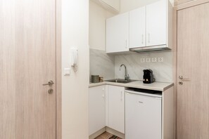 A compact kitchen with white cabinets, a built-in microwave, and a coffee maker. - Moira Apartment by Senaon Urban Living (Iraklio)