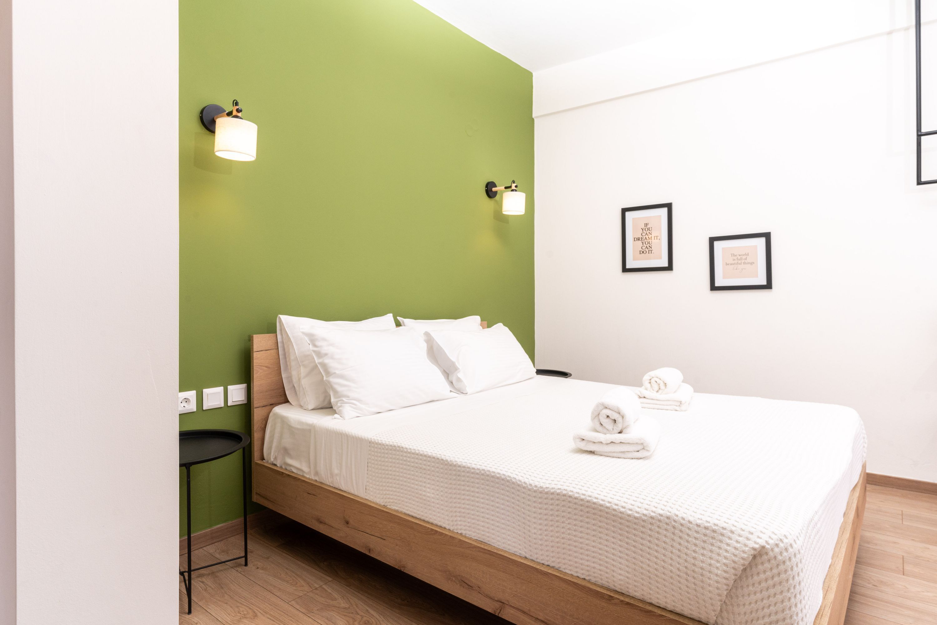 Un lit bien fait, avec du linge de lit blanc, un mur d’accent vert et deux tableaux encadrés accrochés au mur.