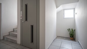 Una escalera moderna y luminosa con una puerta, un ventanal pequeño y una planta en maceta.