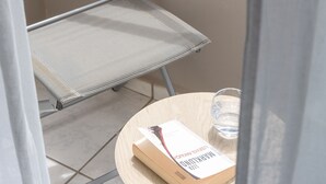Un balcón con una silla de metal y una mesita con un libro y un vaso de agua.