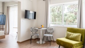 Una habitación moderna con cama, televisor, una mesita con sillas y un ventanal con vistas a árboles.