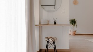 Habitación minimalista con piso de madera, un espejo redondo, un taburete pequeño, una cesta y una planta en maceta.
