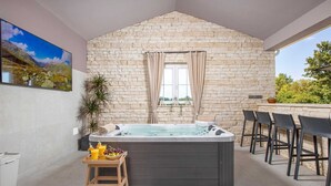 Wellnessbereich mit Steinwand, Whirlpool, Holzschemel mit Getränken und Tisch mit Stühlen.