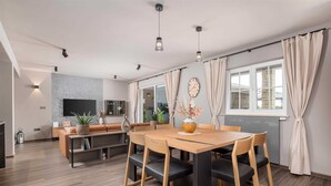 Ein modernes Wohnzimmer mit einem Holzespeisetisch, schwarzen Stühlen, einer Couch und einem an der Wand befestigten Fernseher.