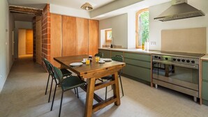 Una cocina moderna con una mesa de comedor de madera, sillas verdes, un horno de acero inoxidable y una ventana con vista a follaje.