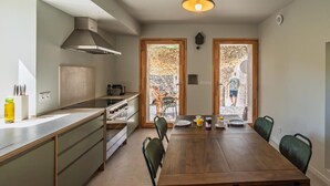 Una cocina moderna con comedor, que incluye una gran mesa de madera, sillas verdes y vistas a través de las ventanas.