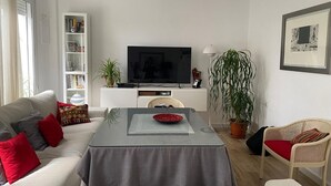 Una sala de estar con un sofá, una mesa de centro, una televisión, una estantería y una planta en maceta.