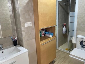 A bathroom with a sink, mirror, wooden cabinet, shower, toilet, and a glass door. - Cozy house in Seville with patio, terrace and 3 bedrooms (Sevilla)