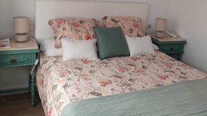 Un dormitorio con colcha estampada, dos almohadas, una manta verde y dos mesitas de noche con lámparas.