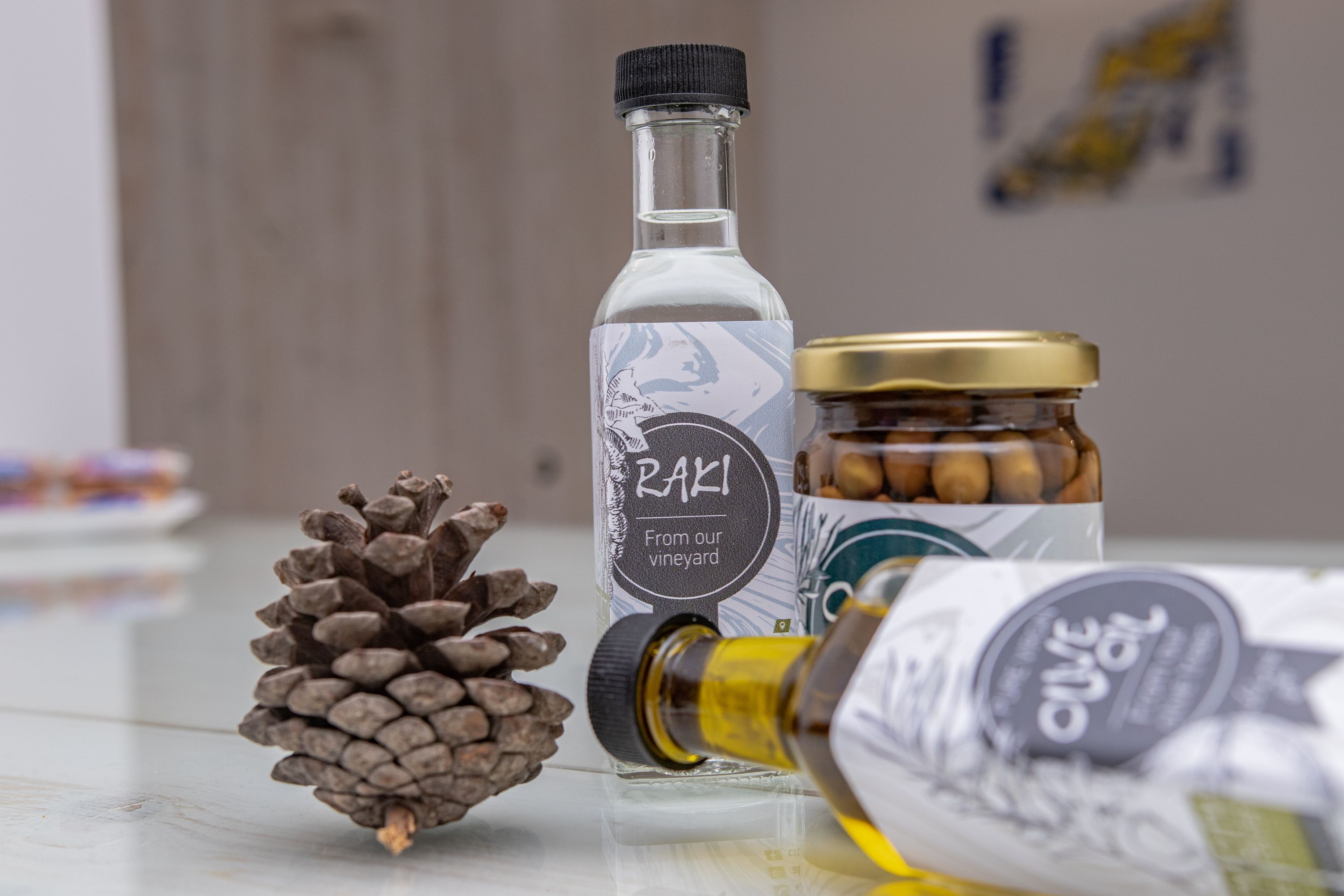 A bottle of Raki, a jar of nuts, and a pine cone on a table.