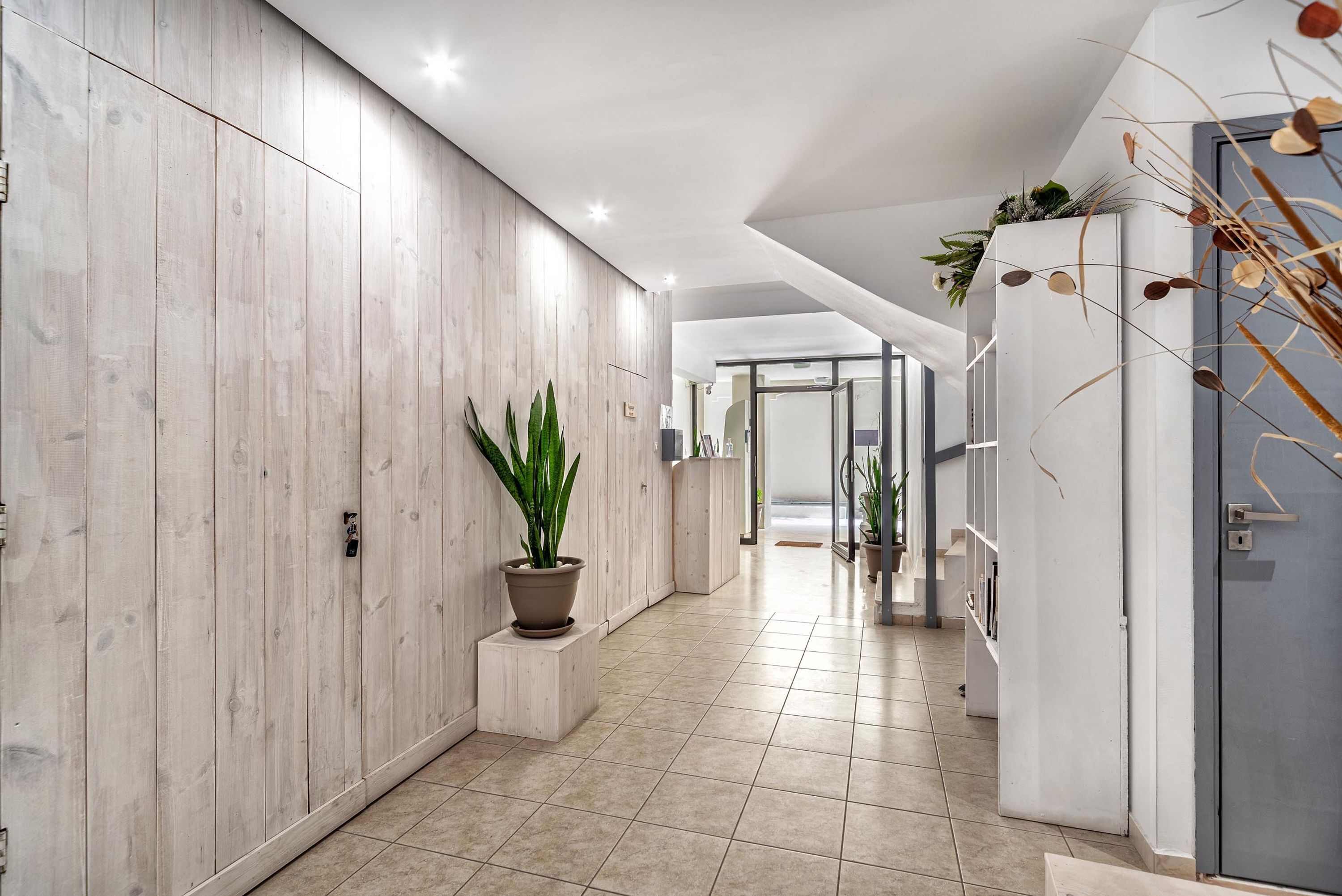 A modern hallway with wooden panel walls, a potted plant, and a tiled floor.