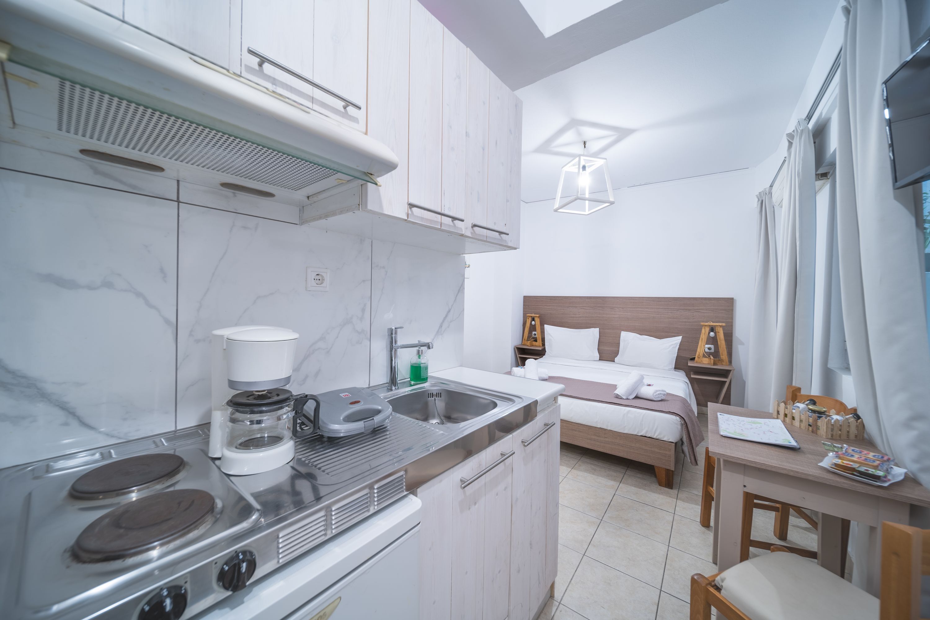 A compact kitchen with a stove, sink, and coffee maker. Adjacent to the kitchen is a small dining area with a table and chairs.