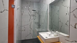 Une salle de bain moderne avec une douche à l’italienne en verre, un lavabo blanc doté d’un plan de toilette en marbre et un grand miroir.