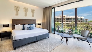 Ett modernt hotellrum med en stor säng, två sängbord, en liten balkong med en stol och utsikt över en byggnad och grönområden.