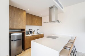 A modern kitchen with wooden cabinets, a stainless steel refrigerator, a built-in oven, a coffee maker, and a white island with bar stools. - Private pool, jungle view, AC and fast WI-Fi (Tulum)