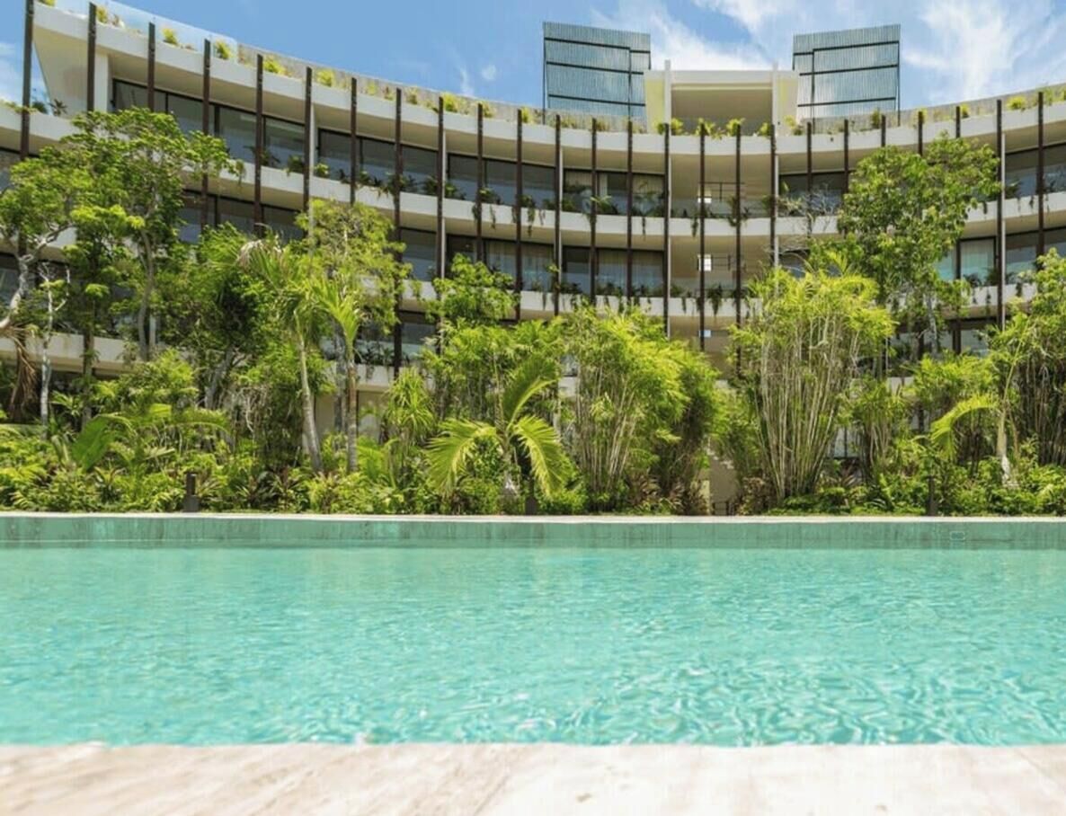 Ein Hotel mit Pool, umgeben von üppiger Vegetation und einem modernen Gebäude mit Balkonen.