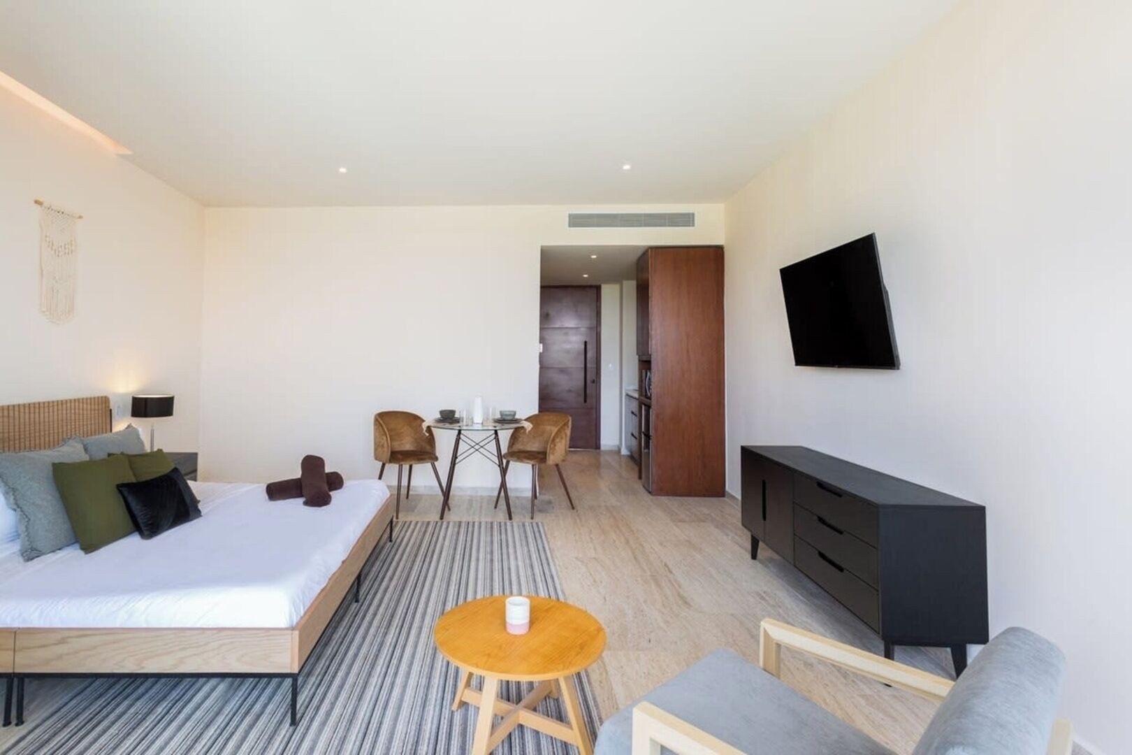 A modern hotel room with a bed, a TV, a desk with chairs, and a small table.
