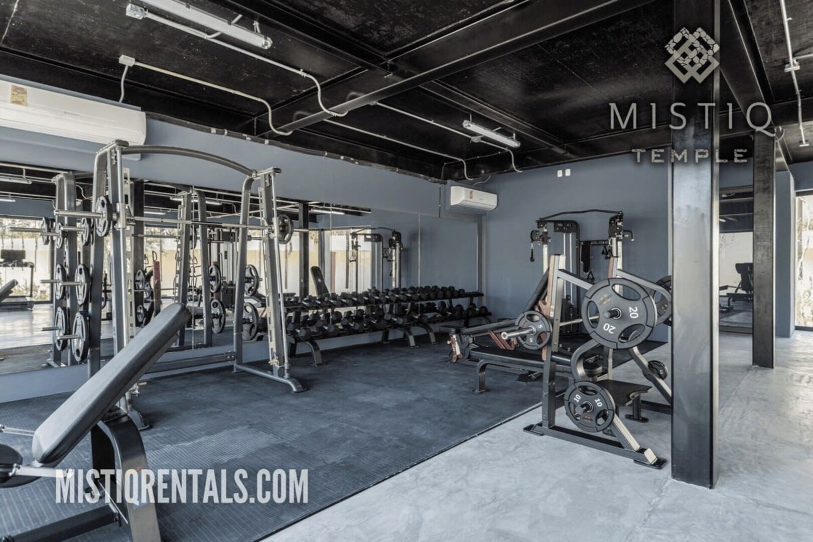 A gym with weightlifting equipment, benches, and dumbbells.
