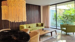 A modern living room with a green sofa, beige armchairs, a black marble coffee table, and a large window with a view of greenery. - Beautiful two bedroom for 6 guests (Tulum)