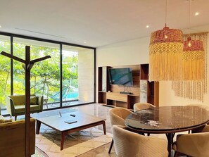 Un salon moderne doté d’une grande porte vitrée donnant sur une piscine, d’une table de salle à manger ronde et d’un téléviseur fixé à un mur en bois.