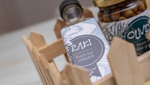 En trækasse med en flaske mærket "Raki Fra vores vingård" og et glas med oliven.