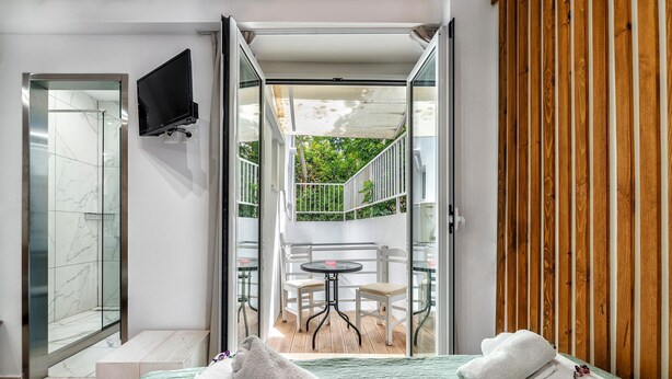 Et hotelværelse med seng, bænk, fjernsyn og en balkon med bord og stole.