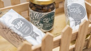 Ein Holzkasten mit Olivenölprodukten, darunter ein Glas und eine Flasche, mit Etiketten, die auf ihren Ursprung in Olivenhainen hinweisen.