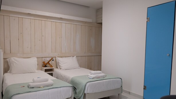 A hotel room with two single beds, a wooden headboard, a blue door, and a marble floor. - City Center Studio |H10 (Iraklio)