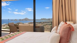 A bedroom with a large window overlooking a coastal view, a bed, a chair, and a view of the sea and buildings. - Enjoy your perfect vacation in this 3 bd (Cabo San Lucas)