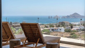 A balcony with two wooden lounge chairs and a view of the sea and buildings. - Enjoy your perfect vacation in this 3 bd (Cabo San Lucas)