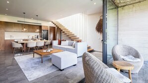 A modern living room with a staircase, a dining area, and a large glass door leading to an outdoor space. - Chic 3BR w/ Private Pool, Gym and Stunning Views (Tulum)