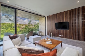 Ein modernes Wohnzimmer mit einem großen Fenster, einem flachbildfernseher, der an einer Holzvertäfelung angebracht ist, und einer gemütlichen Sitzecke mit Sofas und einem Couchtisch.