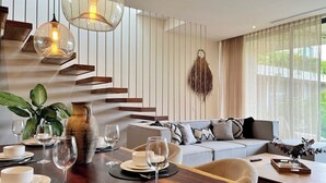 A modern dining area with a wooden table set for a meal, a sofa, and a staircase with wooden steps. - Chic 3BR w/ Private Pool, Gym and Stunning Views (Tulum)