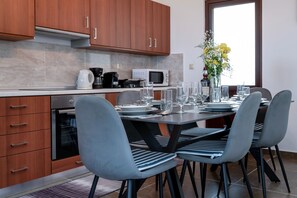A modern kitchen with wooden cabinets, a microwave, and a dining area with a table set for four. - Serenity Luxury Villa in Paradisi Rhodes (Paradisi)