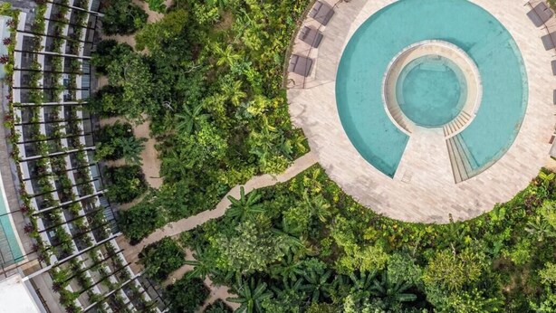 Ein Luftbild eines Resorts mit einem kreisförmigen Pool, umgeben von üppiger Vegetation und einer Reihe von miteinander verbundenen Gebäuden mit Balkonen.