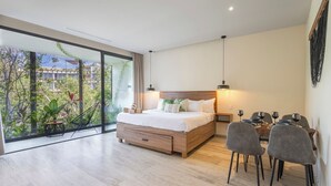 Ein modernes Schlafzimmer mit einem großen Bett, einem Essbereich mit Stühlen und Blick auf Grün durch große Fenster.