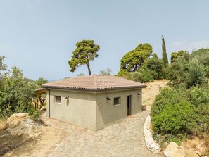 Ein kleines, eingeschossiges Gebäude mit Ziegeldach, umgeben von natürlicher Vegetation und einem gepflasterten Eingangsbereich.