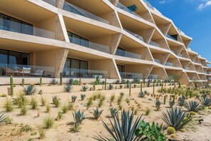 Ein modernes Hotel mit einer geometrischen Fassade, mehreren Balkonen und einem Wüstenpflanzengarten mit Kakteen.