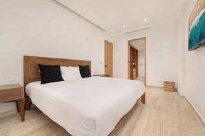 Ein modernes Schlafzimmer mit einem Holzkopfteil, einem großen Bett mit weißer Bettwäsche, einem Nachttisch, einem Holzschrank und einem Bild an der Wand.