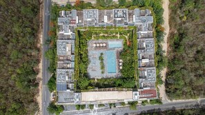 Vue aérienne d’un complexe hôtelier doté d’une piscine centrale, de nombreuses chambres et d’une végétation luxuriante.