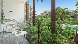 Un balcón con mesa y silla, rodeado de exuberante vegetación y una piscina.