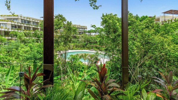 Un jardín exuberante con piscina, rodeado de follaje denso y edificios modernos al fondo.