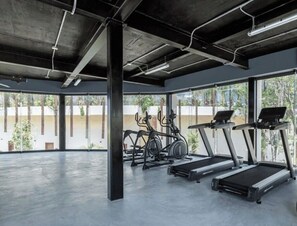 Ein modernes Fitnessstudio mit Laufbändern, Crosstrainern und einem großen Fenster mit Blick ins Freie.