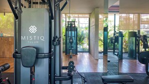 Ett gym med träningsutrustning, en bänk och ett stort fönster med utsikt över grönområden.